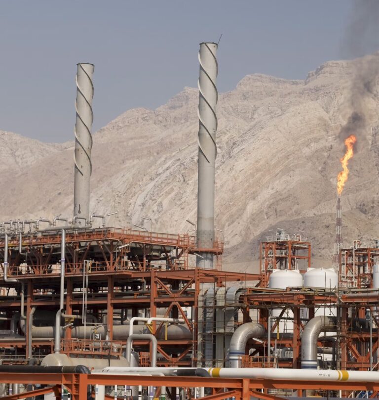 Flames of gas flaring at an Iranian oil and gas complex with desert mountains in the background, illustrating the pressure on Iran’s oil network.