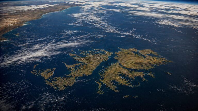 Aerial photograph of the Falkland Islands in the South Atlantic Ocean, with a rugged green coastline and open sea.